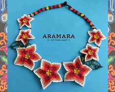 a crocheted necklace with red flowers and butterflies on it, in front of a blue background