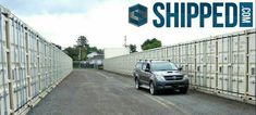 a car is parked in front of some shipping containers on the side of a road