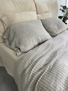 an unmade bed with two pillows and a plant in the corner next to it