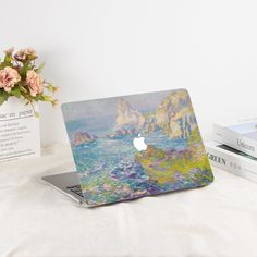 an apple laptop computer sitting on top of a white table next to books and flowers