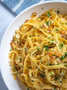 a white bowl filled with pasta covered in parmesan cheese and garnished with herbs