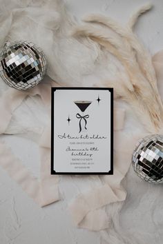 a white and black wedding card with silver disco balls on the ground next to it