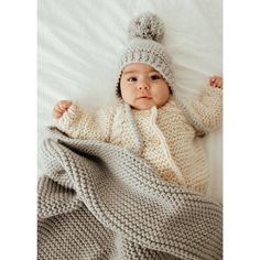 a baby is laying down wearing a knitted hat and sweater with a pom - pom on it's head