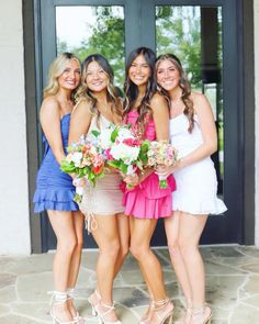 four beautiful young women standing next to each other in front of a door holding bouquets