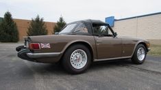 a brown sports car parked in a parking lot next to a building with a british flag on the roof