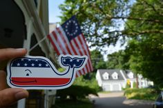 a person holding up a sticker with a whale on it's side and an american flag in the background