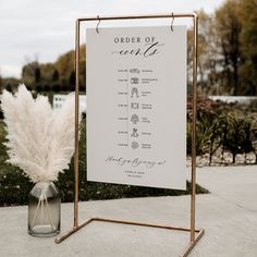 a white sign sitting on top of a sidewalk next to a vase filled with flowers