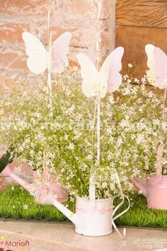 flowers in watering cans with fairy wings on them and grass growing out of the top