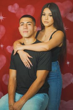 a man and woman sitting next to each other in front of a red background with hearts