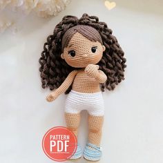 a crocheted doll is posed on a white surface with flowers in the background