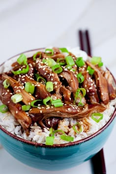 a blue bowl filled with rice covered in meat and green onions