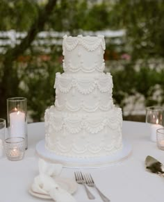 a white wedding cake sitting on top of a table next to silverware and candles