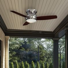 a ceiling fan on the outside of a home's porch with trees in the background