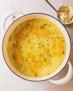 a bowl of soup with corn on the cob in it and a spoon next to it