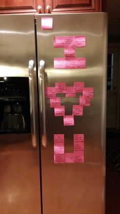 a metallic refrigerator with pink sticky notes on the front and side of it, sitting in a kitchen