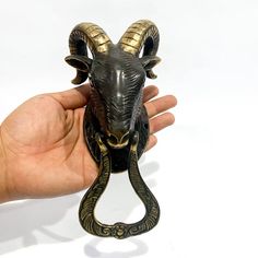 a hand holding a black and gold statue of a ram head with horns on it's back