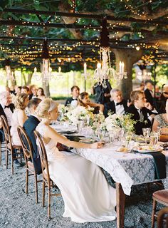 a bride and groom sitting at a long table in front of an outdoor dining area