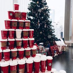 a large stack of coffee cups sitting in front of a christmas tree