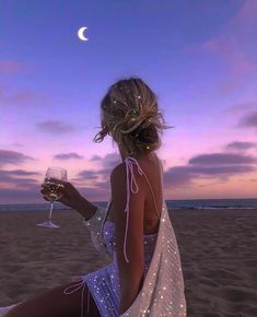 a woman sitting on top of a sandy beach holding a glass of wine in her hand