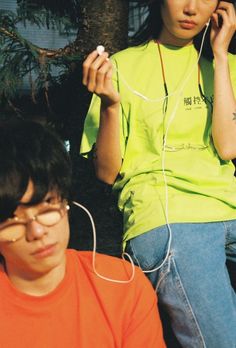 two people sitting next to each other with ear buds in their ears and one person on the phone