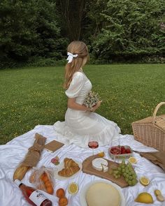 a woman in white dress sitting at a picnic table with fruit and bread on it