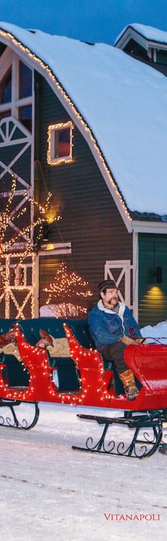 a man riding on a sled pulled by two dogs in front of a barn