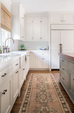 a large rug in the middle of a kitchen with white cupboards and drawers on both sides