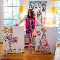 a woman standing next to two paintings on the floor