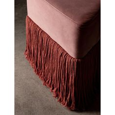 a pink velvet bench with fringes on the bottom and back end, in front of a dark background