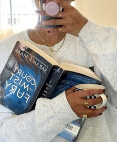 a woman reading a book while holding a coffee mug in her hand and drinking from a cup