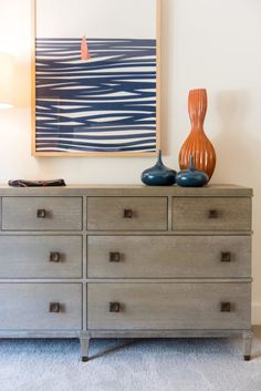 a dresser with two vases on top of it in front of a painting and lamp