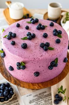 a cake with blueberries on it sitting on top of a wooden platter next to other desserts