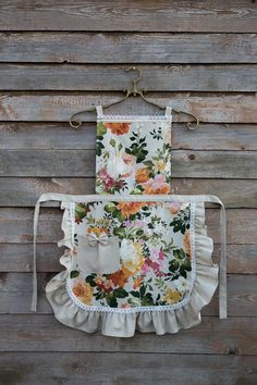 two aprons with flowers on them hanging against a wooden wall in front of a wood paneled wall