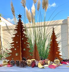 three metal christmas trees sitting on top of a table next to plants and cones in front of a building