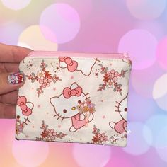 a hello kitty purse with pink flowers and bows on the front is being held up by a woman's hand