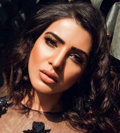 a close up of a woman with long dark hair wearing a sheer top and earrings