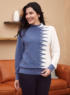 a woman standing in front of a couch wearing a blue and white sweater