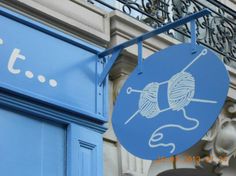 a blue sign hanging from the side of a building next to a bicycle rack with yarn on it