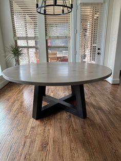 a round dining table sits in the middle of a room with wooden floors and windows