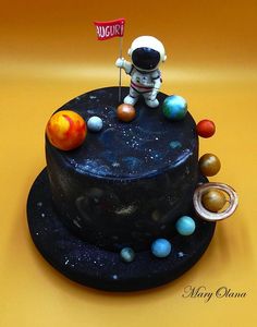 a small cake with an astronaut on top and planets around it, sitting on a yellow surface