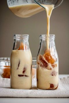 two glass jars filled with liquid and some food in them on top of a table