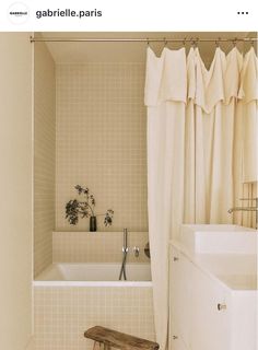 a white bath tub sitting next to a wooden bench in a bathroom under a shower curtain