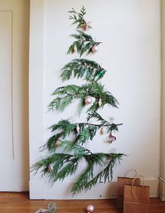 a christmas tree with ornaments hanging from it's branches in front of a white wall