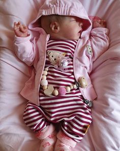 a baby laying on top of a bed wearing a pink and white striped outfit with teddy bears