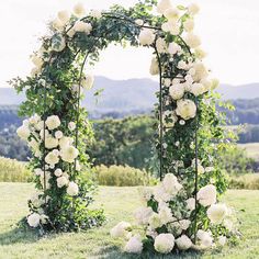 an outdoor wedding ceremony with white flowers and greenery on the grass in front of mountains