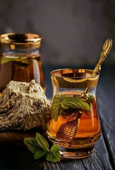 a glass cup filled with tea next to two jars full of honey and some leaves