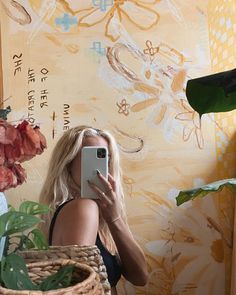 a woman taking a selfie in front of a wall with flowers and plants on it