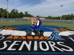 two graduates standing in front of the senior sign on the field at their graduation ceremony