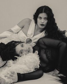 two women are laying on the floor posing for a black and white photo with feathers