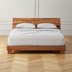 a bed with white sheets and pillows on top of it in a wooden floored room